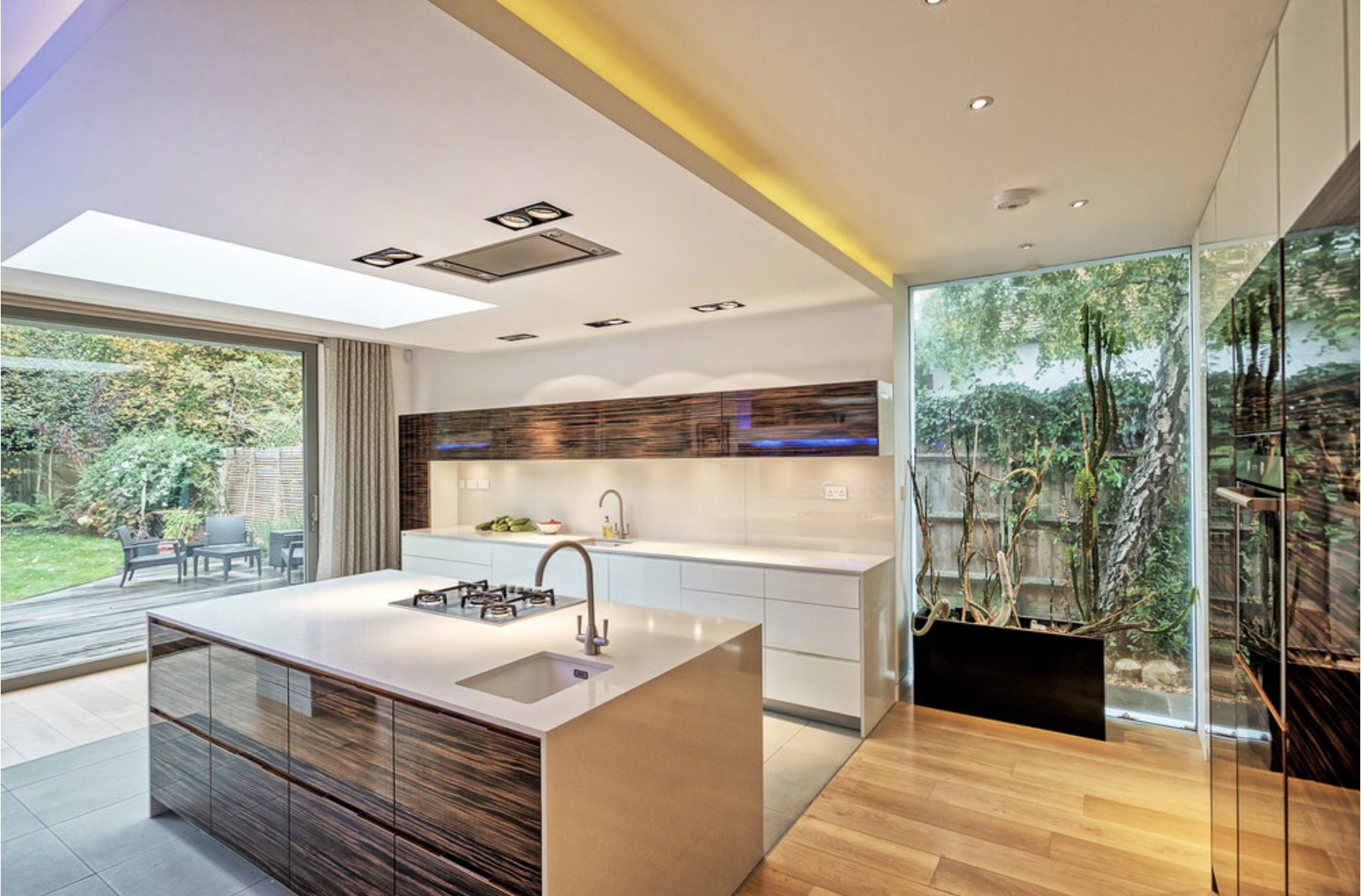 Modern London kitchen extension by PM Modern Construction — ebony cabinetry, white quartz worktop, glass garden wall